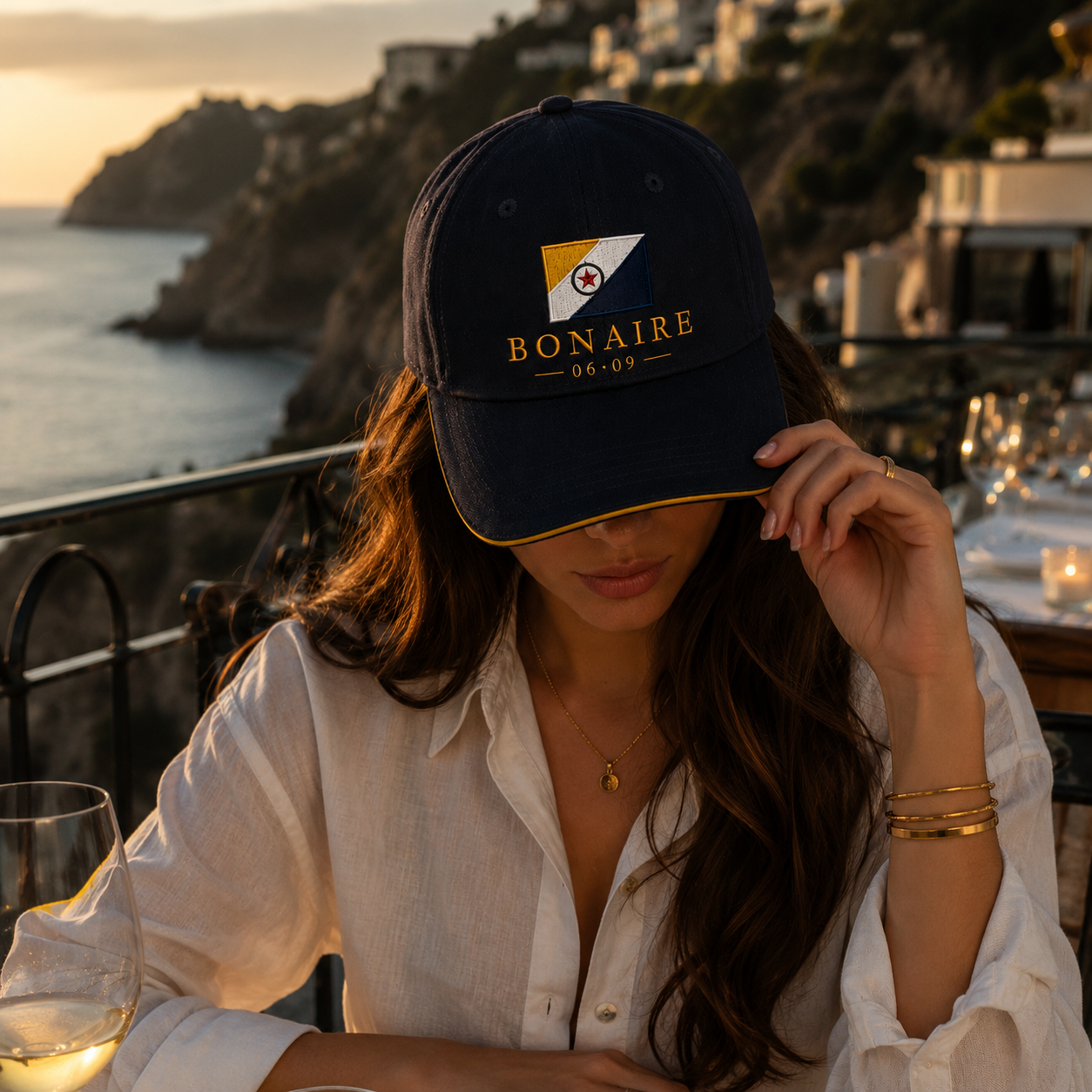 A woman wearing a black baseball cap with a circular embroidered design on the front. The design features the outline of the island of Bonaire in light blue, with the white text 'BONAIRE DAY' in the center of the map